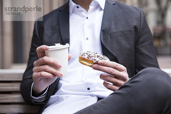 Die Hände eines Geschäftsmannes mit Doughnut und Kaffee zum Mitnehmen  Nahaufnahme