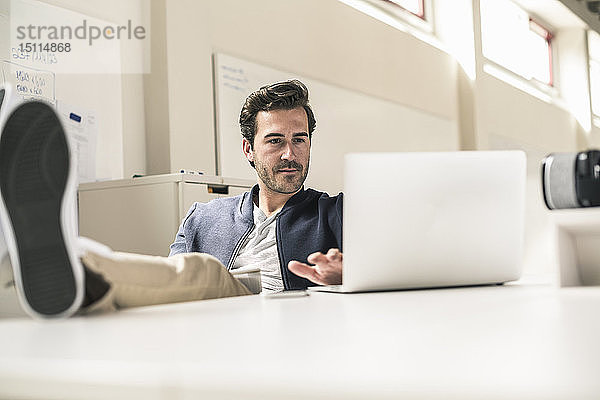 Junger Geschäftsmann arbeitet entspannt in modernem Büro  Laptop mit den Füßen auf dem Schreibtisch