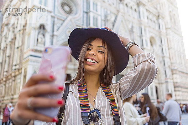 Italien  Florenz  Piazza del Duomo  Porträt eines glücklichen jungen Touristen  der sich mit einem Smartphone selbstständig macht