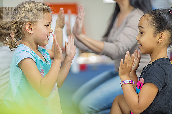 Glückliche Kinder und Vorschullehrerin klatschen im Kindergarten in die Hände