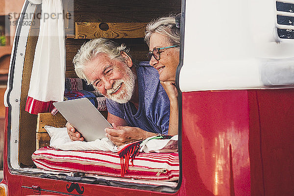 Älteres Ehepaar reist in einem Oldtimer-Van  liegt im Kofferraum und benutzt ein digitales Tablett