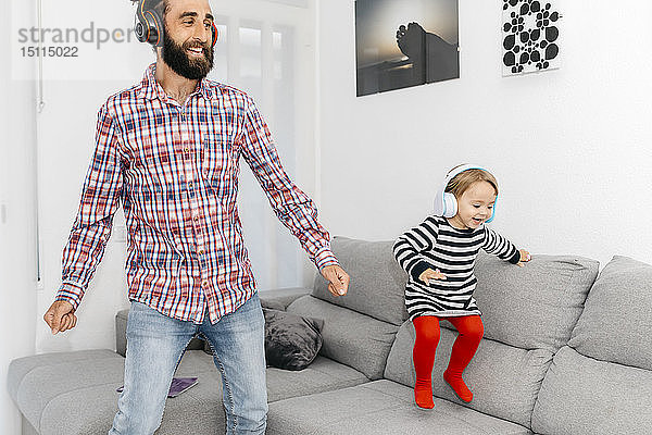 Vater und kleine Tochter tanzen im Wohnzimmer  während sie mit Kopfhörern Musik hören