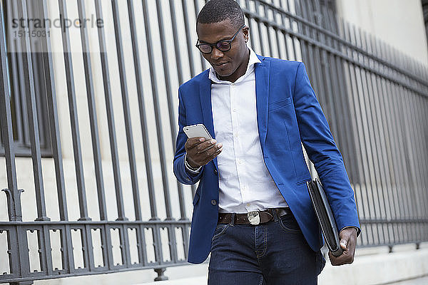 Junger Geschäftsmann in blauer Anzugsjacke und mit Smartphone