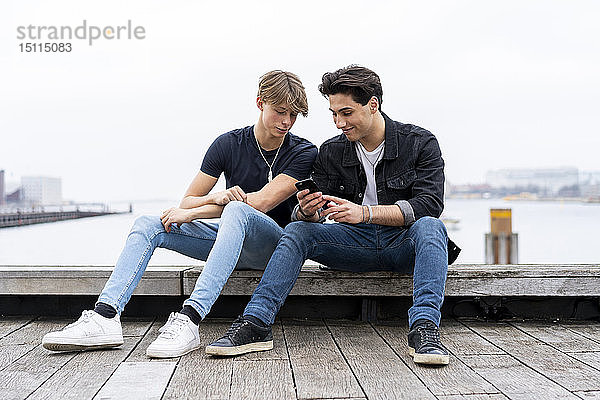 Dänemark  Kopenhagen  zwei junge Männer sitzen am Wasser und telefonieren