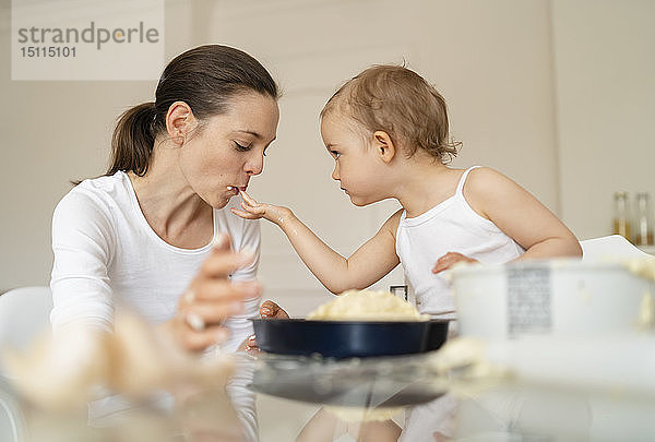 Kleines Mädchen  das seine Mutter füttert  während es zu Hause in der Küche einen Kuchen backt