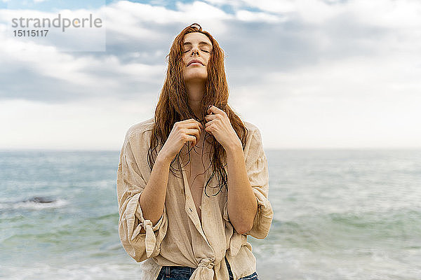 Porträt einer rothaarigen jungen Frau mit Nasenpiercing vor dem Meer stehend