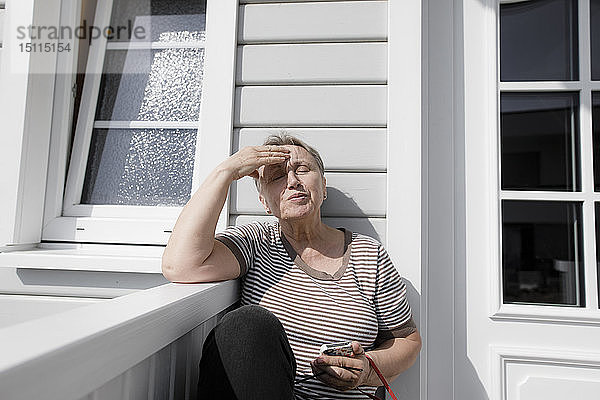 Entspannte ältere Frau sitzt auf der Veranda im Sonnenschein