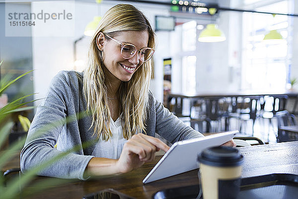 Junge Frau benutzt ihr digitales Tablett beim Kaffeetrinken im Café