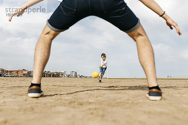 Mann und Junge spielen Fussball am Strand