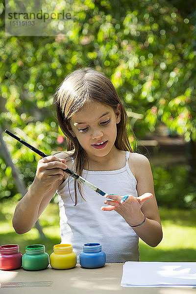 Mädchen im Garten malt ihre Hand mit blauer Farbe