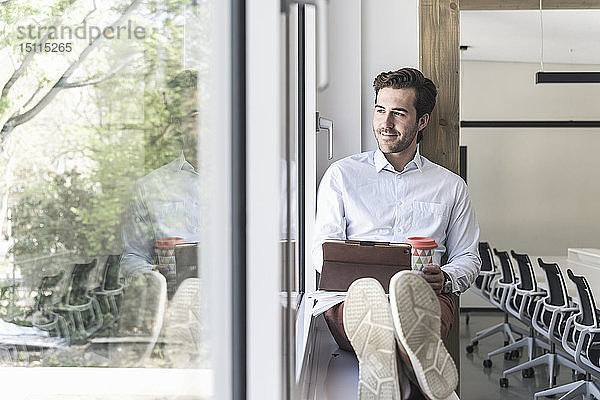Junger Geschäftsmann sitzt auf der Fensterbank und benutzt ein digitales Tablett