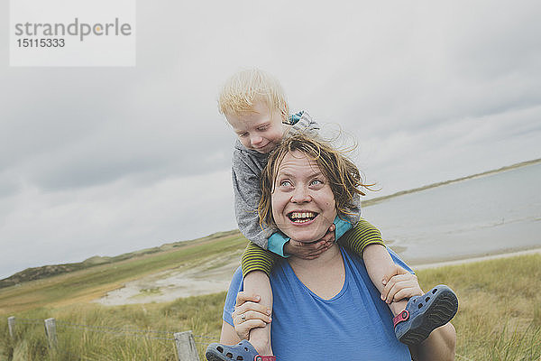 Porträt einer glücklichen Mutter  die ihre kleine Tochter auf den Schultern trägt  Sylt  Deutschland