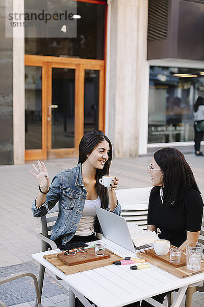 Zwei Freunde sitzen mit Laptop in einem Straßencafé zusammen
