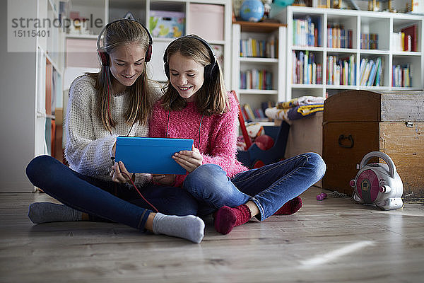 Geschwister  die zu Hause mit ihren digitalen Tabletts spielen und auf dem Boden sitzen