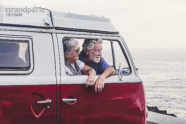 Älteres Ehepaar reist in einem Oldtimer-Van und schaut auf das Meer