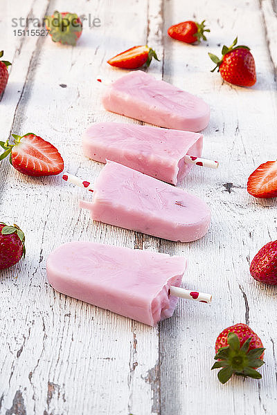 Hausgemachte Erdbeer-Joghurt-Eislollys mit frischen Erdbeeren auf weißem Holz