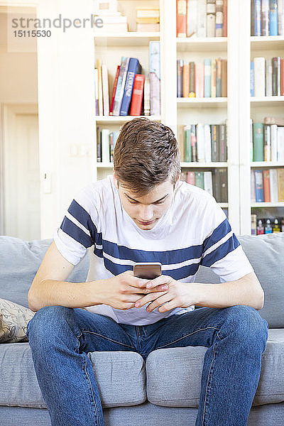 Teenager  der zu Hause auf der Couch sitzt und sein Handy benutzt