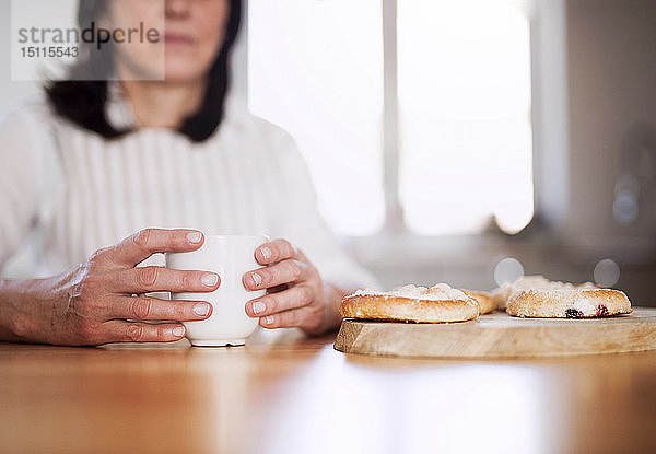 Reife Frau sitzt am Küchentisch und trinkt Kaffee