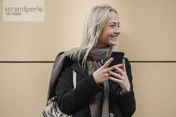 Lächelnde junge Frau mit Handy an der Wand