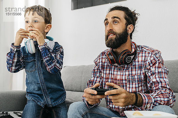 Porträt von Vater und Sohn auf der Couch beim Computerspiel