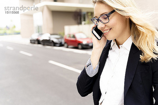 Lächelnde junge Geschäftsfrau am Telefon beim Überqueren der Straße