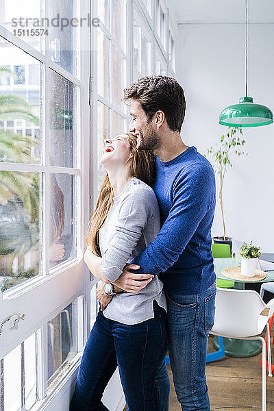 Glückliches  liebevolles Paar  das sich zu Hause am Fenster umarmt
