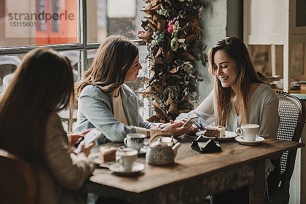 Drei glückliche junge Frauen mit Handy-Treffen in einem Cafe
