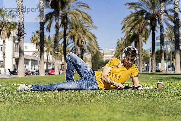 Spanien  Barcelona  auf dem Rasen liegender Mann in der Stadt mit Kopfhörern und Notebook