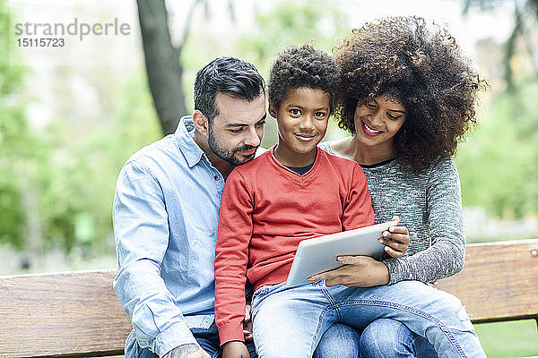 Familie sitzt auf einer Parkbank und verwendet ein digitales Tablett