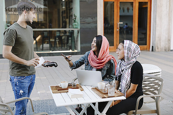 Junge Frau bezahlt bargeldlos mit Smartphone in einem Café