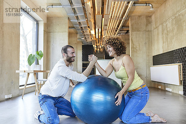 Glücklicher Mann und Frau beim Armdrücken auf dem Fitnessball im modernen Büro