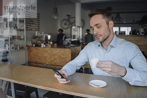 Erfolgreicher Geschäftsmann sitzt im Café  trinkt Kaffee  benutzt Smartphone