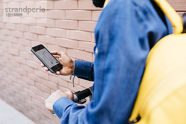 Mann mit Rucksack und E-Scooter mit Navigations-App auf seinem Mobiltelefon  Teilansicht