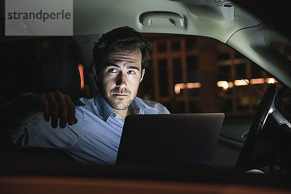 Junger Mann mit Laptop nachts im Auto