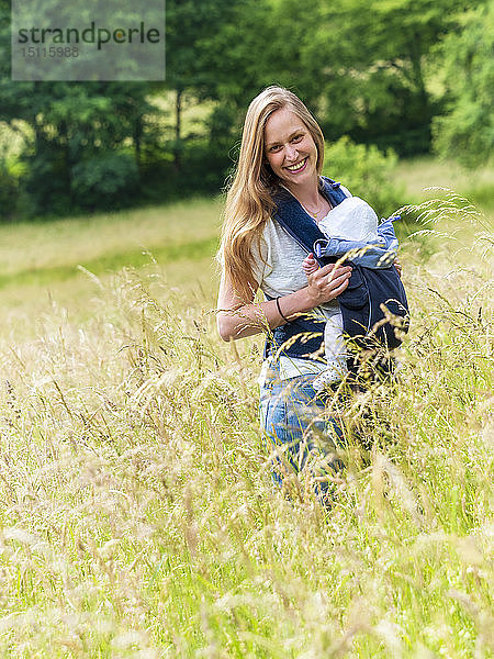 Porträt einer glücklichen Mutter  die ihre kleine Tochter im Tragetuch in der Natur trägt