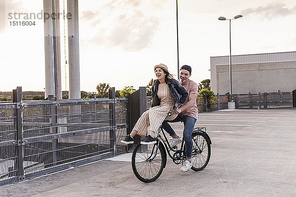Glückliches junges Paar zusammen auf einem Fahrrad auf dem Parkdeck