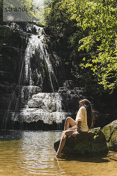 Junge Frau sitzt auf einem Felsen an einem Wasserfall  Garrotxa  Spanien