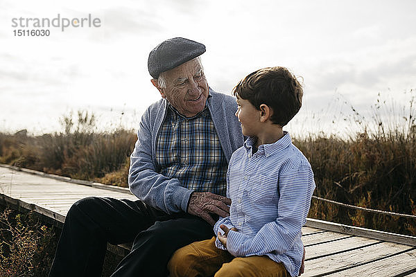 Glücklicher Großvater sitzt mit seinem Enkel an der Strandpromenade und sieht einander an