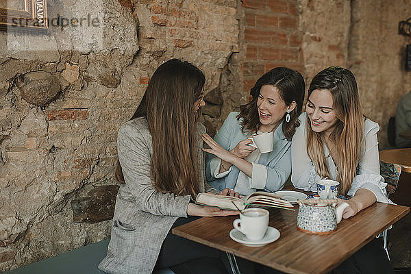 Drei glückliche junge Frauen haben Spaß beim Lesen eines Buches in einem Cafe