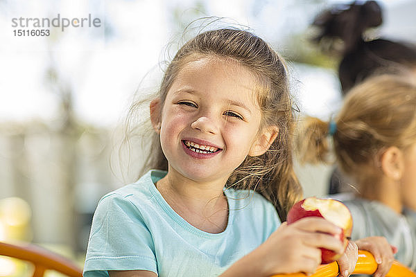 Porträt eines glücklichen Mädchens  das im Kindergarten einen Apfel isst
