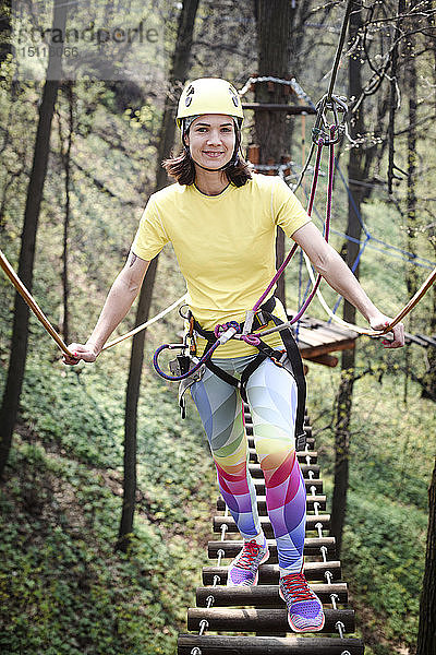 Junge Frau mit gelbem T-Shirt  Helm und Regenbogenhose in einem Seilgarten