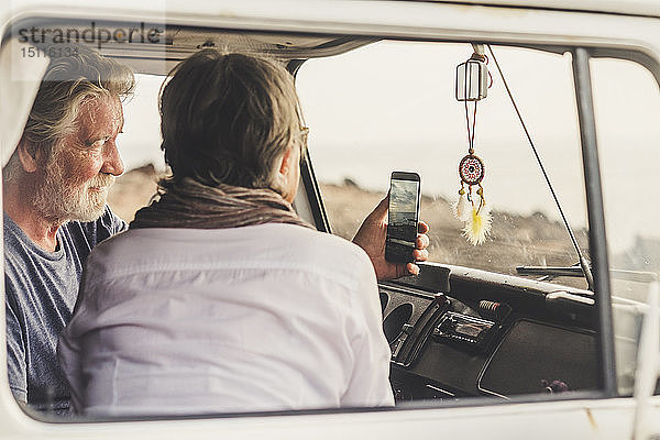Älteres Ehepaar reist in einem Oldtimer-Van und benutzt ein Smartphone