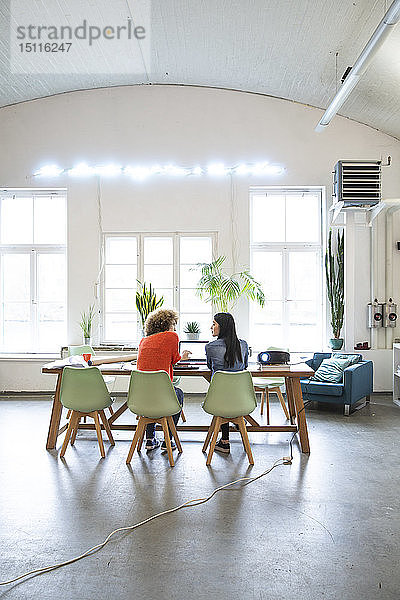 Rückansicht von zwei Frauen  die am Tisch in einem modernen Büro arbeiten