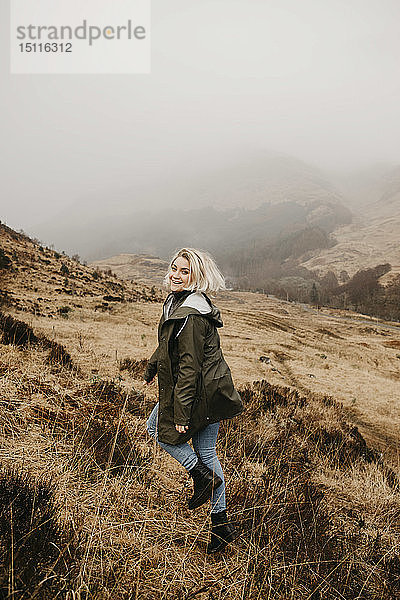 Großbritannien  Schottland  Hochland  glückliche junge Frau läuft in ländlicher Landschaft