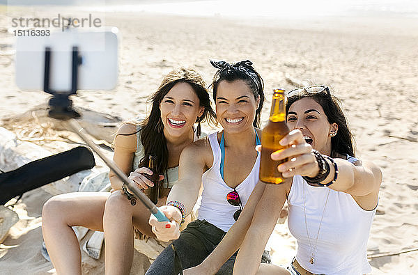 Glückliche Freundinnen mit Bierflaschen  die sich am Strand ein Selfie gönnen