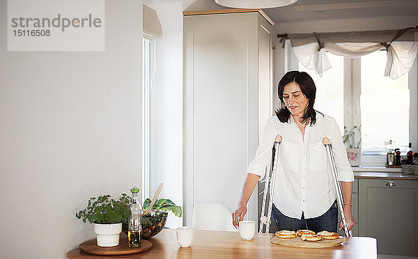 Reife Frau mit Krücken  allein zu Hause  Küchentisch decken