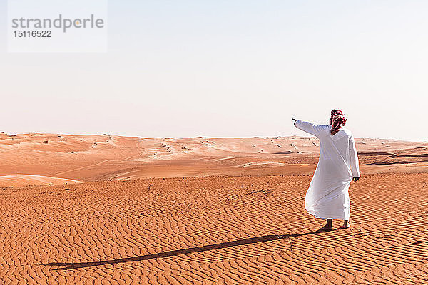 Beduine in Nationaltracht in der Wüste stehend  auf Distanz zeigend  Wahiba Sands  Oman