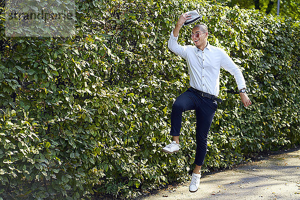 Glücklicher junger Mann springt an einer Hecke herum