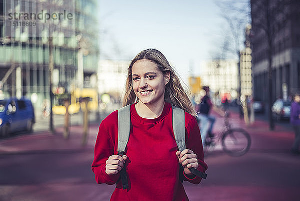Deutschland  Berlin  Porträt einer lächelnden jungen Frau mit Rucksack in der Stadt