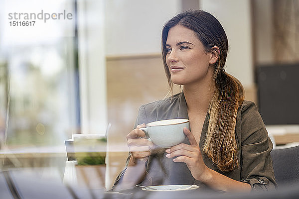 Junge Geschäftsfrau mit Kaffeetasse in einem Café  durch ein Fenster gesehen